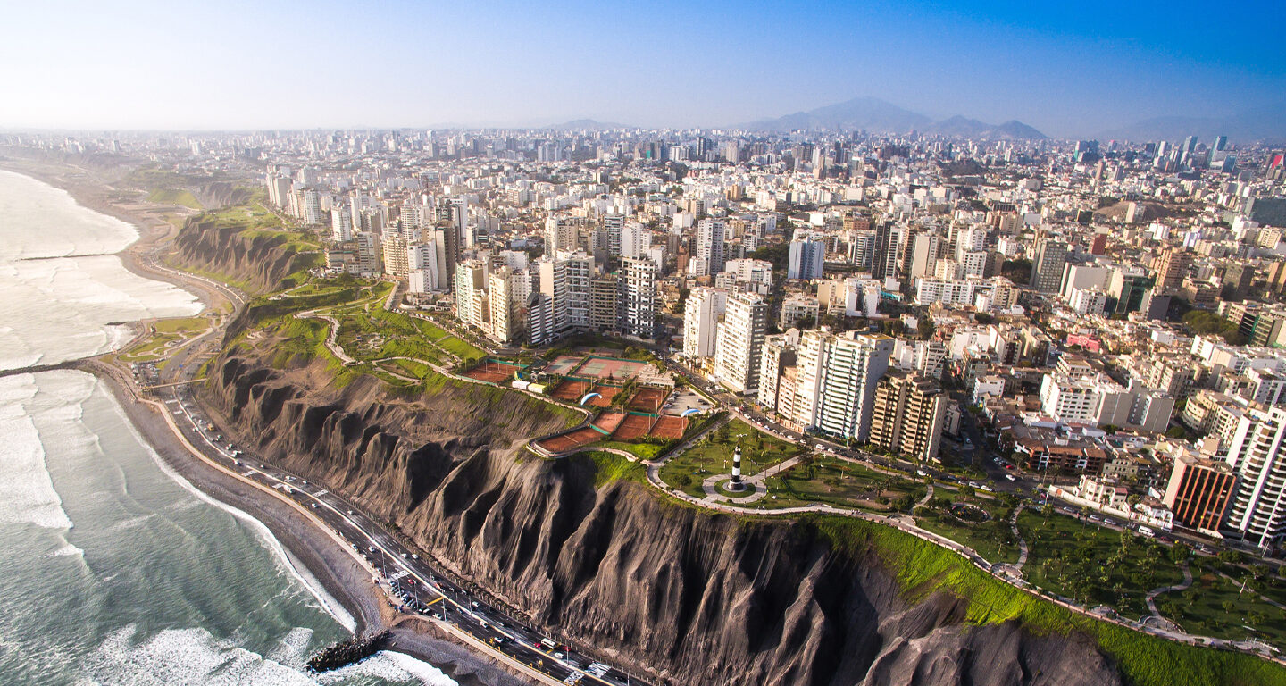 Aerial view of Peru coastline with waves crashing along the beach with cliff and skyscrapers