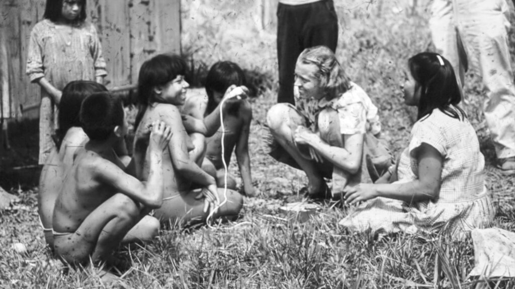 Elisabeth Elliot sits with Waorani women, one of whom is examining her Dictaphone.