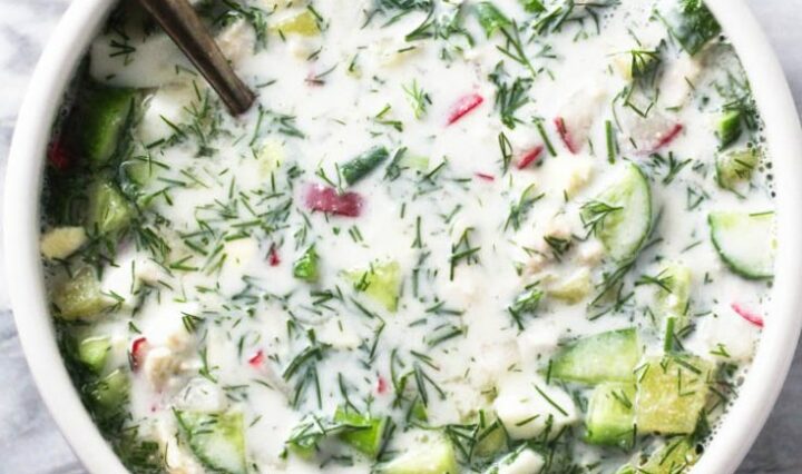 An aerial view of a bowl of okroshka, with cucumbers and other vegetables.