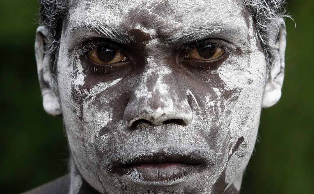 Портрет отблизо на млад коренно население, който гледа сериозно в камерата с бяла боя, покриваща лицето му