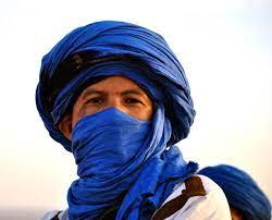 A Berber man stares right into the camera, wearing a deep blue tagelmust around his head as a turban and over his face.