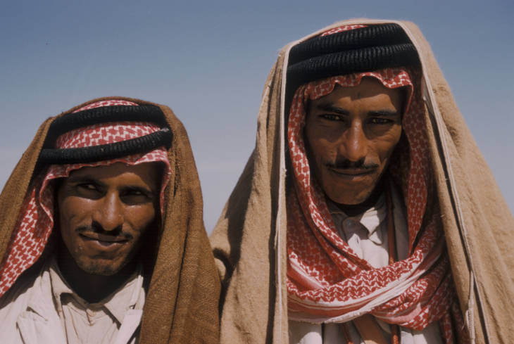 Two Arab men wearing read and white keffiyeh look into the camera.