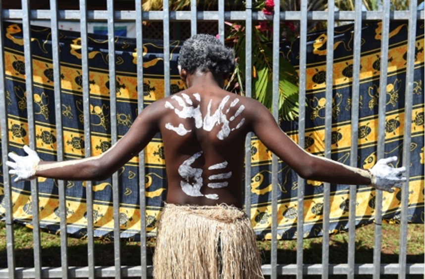 Аборигенско момче стои с разтворени ръце към оградата на бара с бял отпечатък на ръката, боядисан назад към камерата