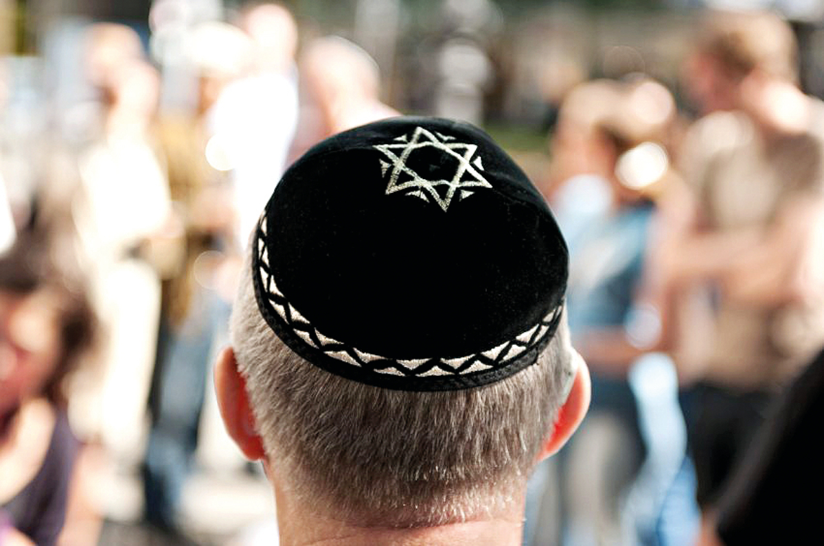 The back of a Jewish man's head as he stands in a crowd, wearing a kippah with the Star of David on it.