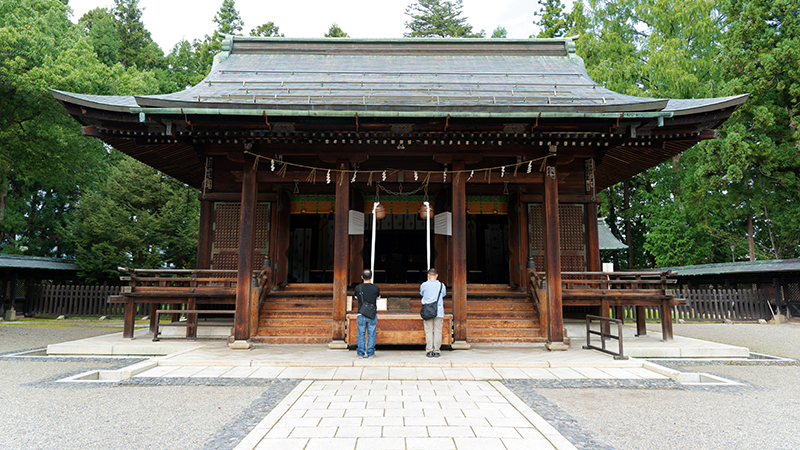 A Japanese shrine for one of the deceased samurai, with two people in front paying their respect to bring life to his legacy as a samurai in feudal Japan.