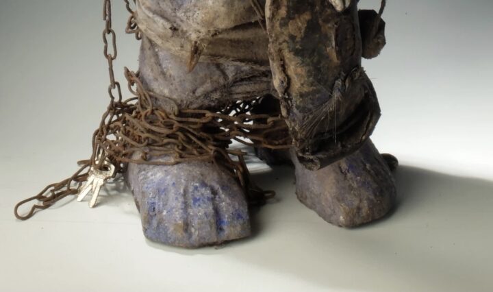 Closeup on feet of evil statue that is wrapped in rusted chains with keys to left of feet