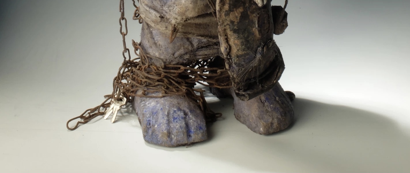 Closeup on feet of evil statue that is wrapped in rusted chains with keys to left of feet