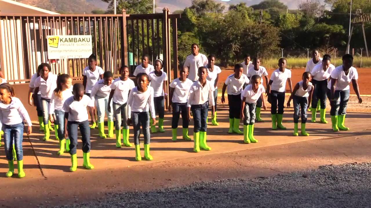 Børn i en skole, der bruger gumboot dans som og uddannelsesmæssigt redskab iført hvide skjorter, jeans og gule oots i skolegården