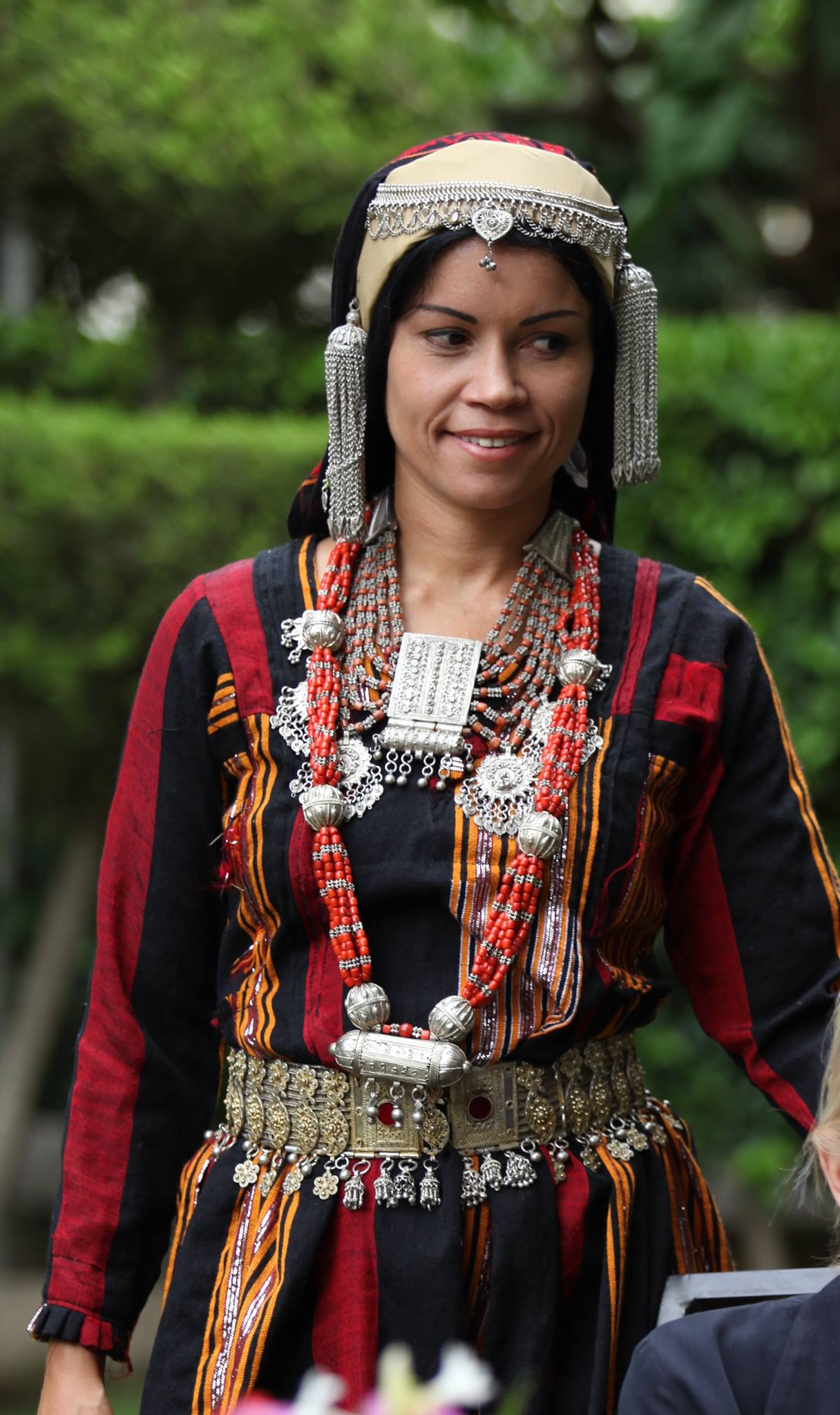 הכותבת מדגמנת את לבוש הכלות הסנאני המסורתי עם כיסוי הראש, חגורת הכסף והשרשראות בגן ירוק