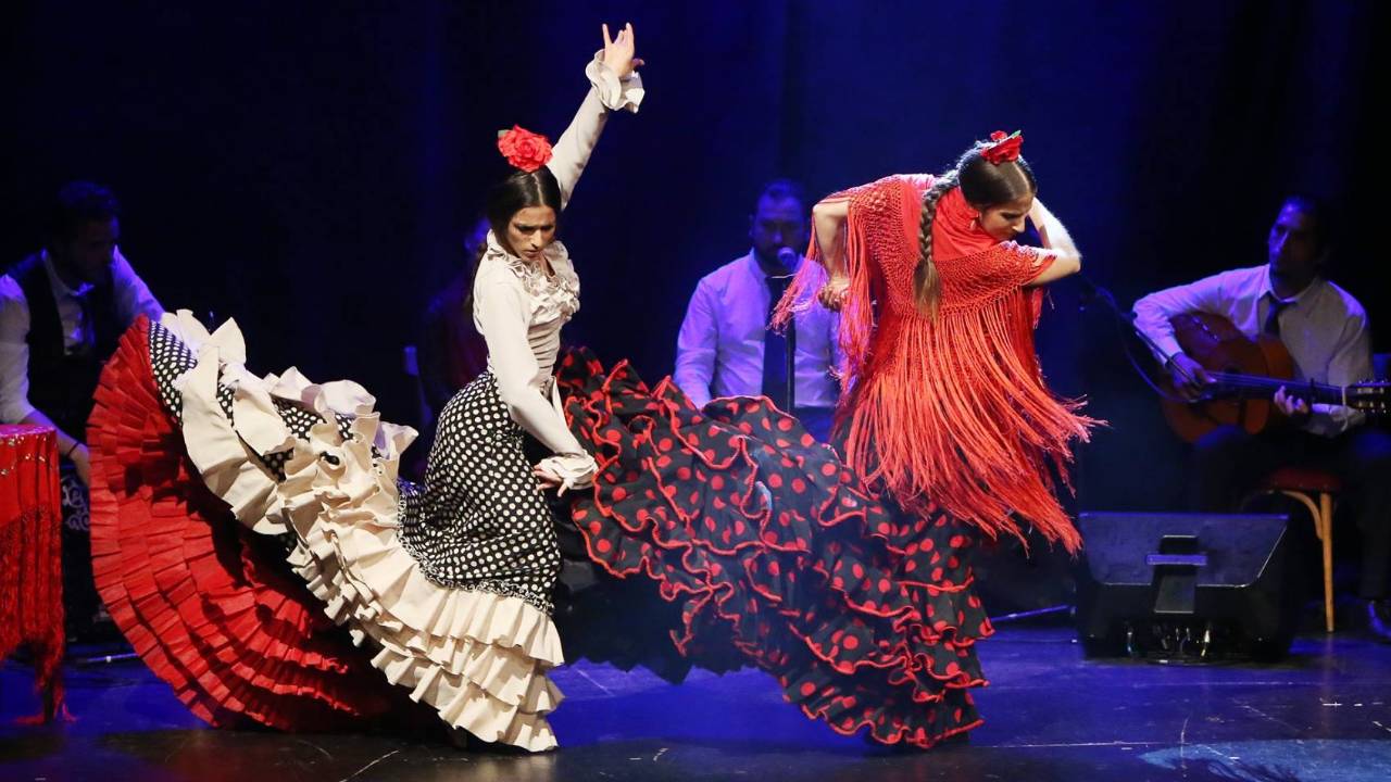 et farvet billede af flamencodansere, der optræder på scenen ledsaget af levende musik