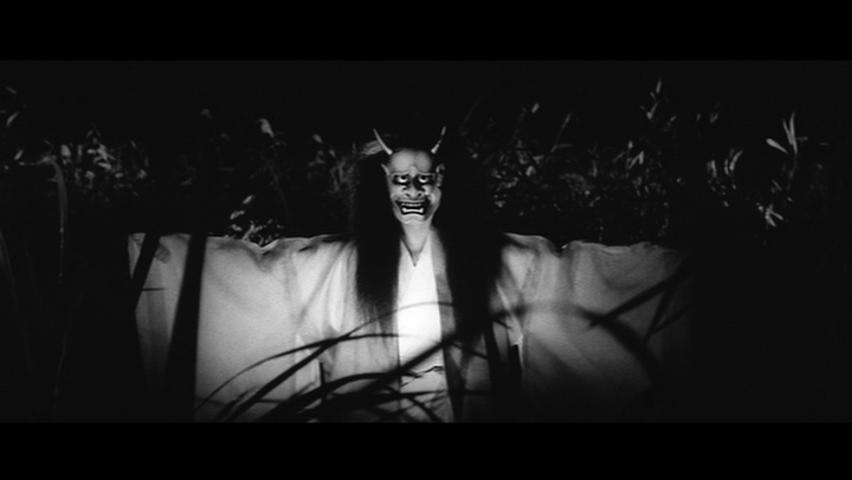 a black and white picture of a scene from Onibaba, where a woman, wearing a samurai mask standing among the bushes,opening her arms widely 