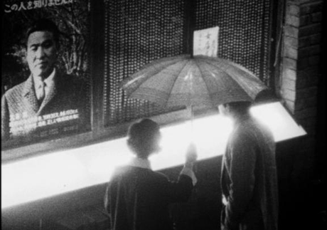 a black and white picture of a couple standing under an umbrella, looking at the photo of the vanished man 