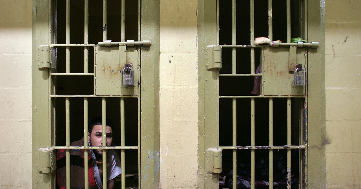 En cremefarvet fængselsvæg med en mand, der sidder bag den nederst til venstre