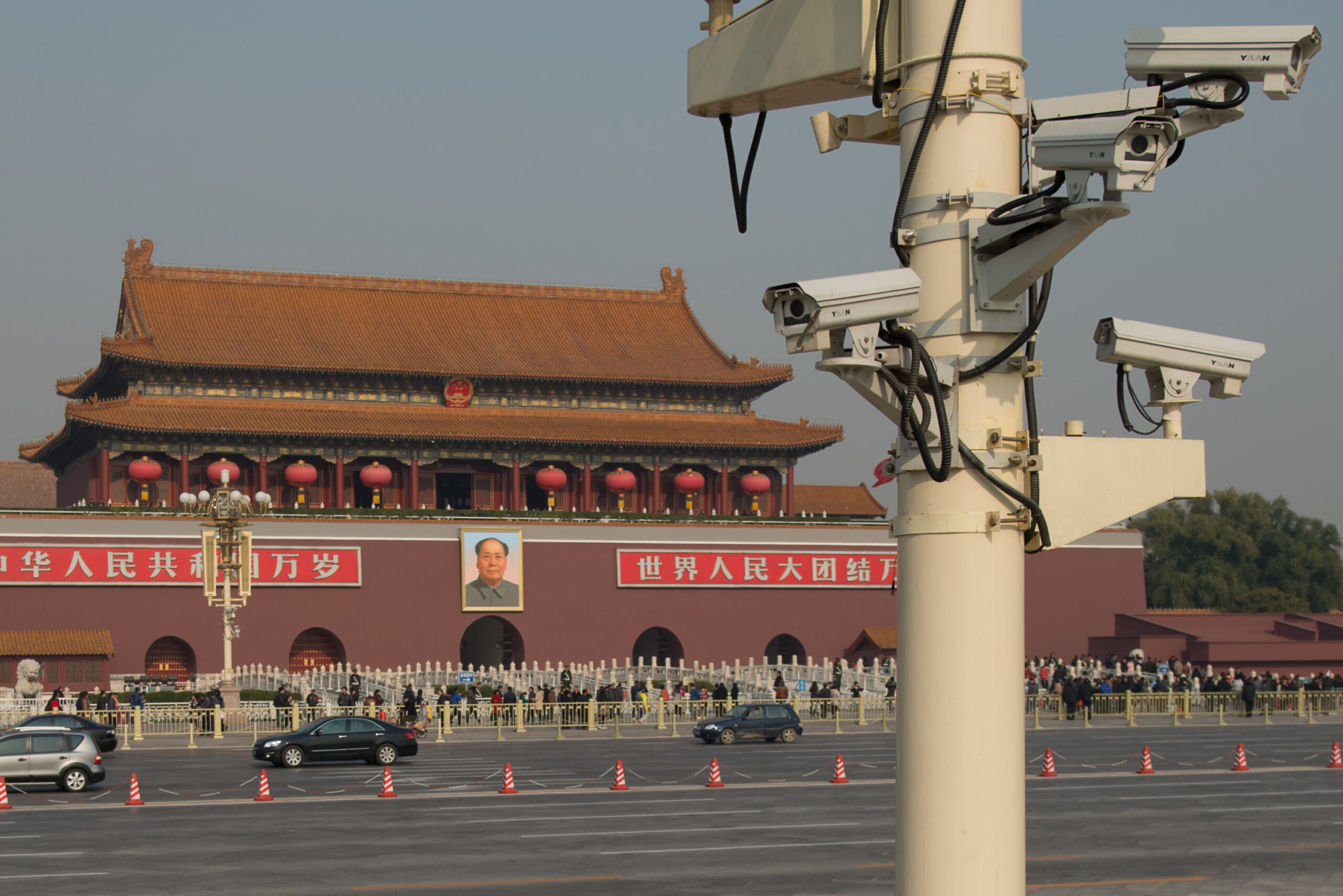 Surveillance cameras looking out over Tiananmen Square in Beijing, China. There is a distant poster of Mao Zedong.