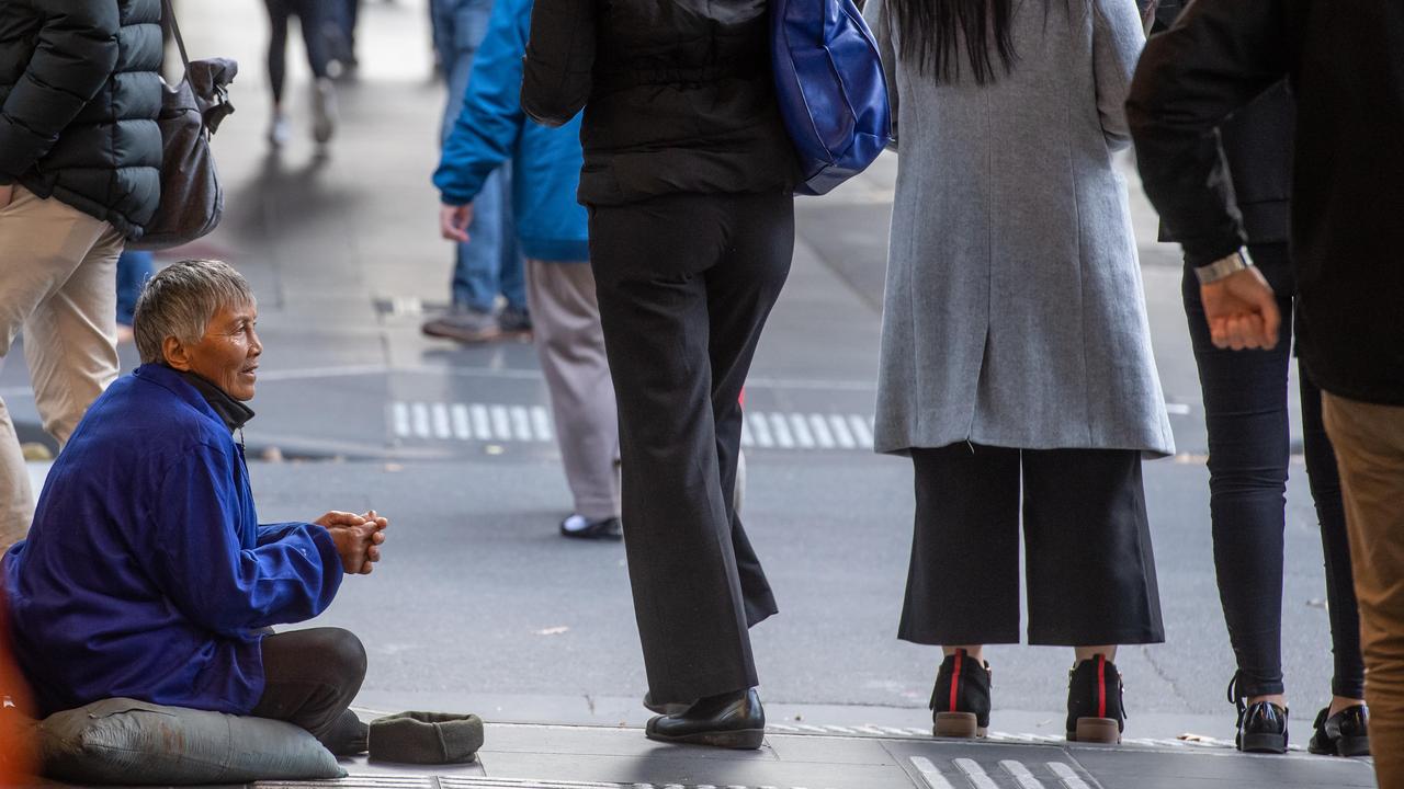 Професионален просяк встрани от улицата вдига ръце за пари, докато хората минават