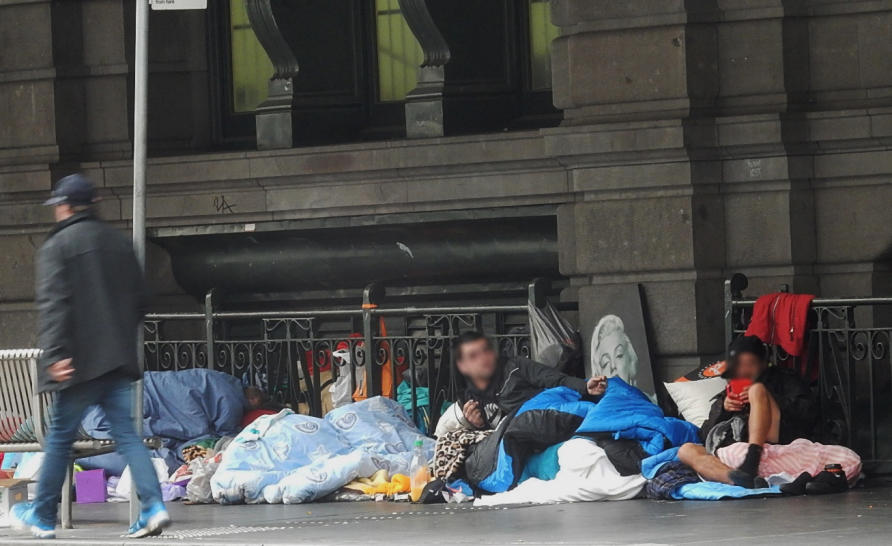 Петима бездомни, увити в спални чували, седят на пода на бетон до каменна стена