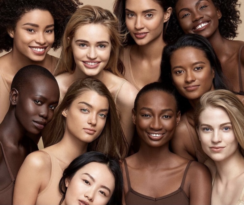 Women of color and white models randomly lined up and smiling in front.
