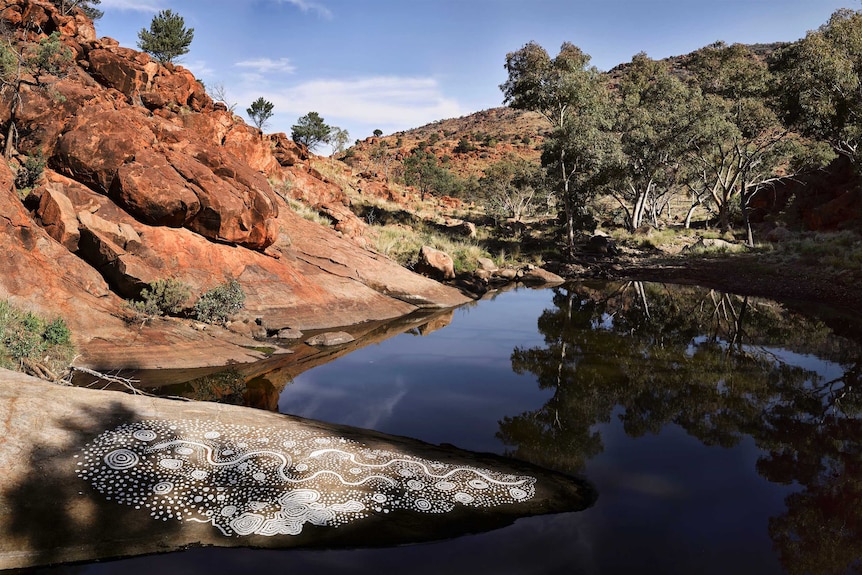 en indfødt australier Dreamtime kunstværk på en klippe ved siden af ​​et fredeligt vandhul midt i den australske ørken.