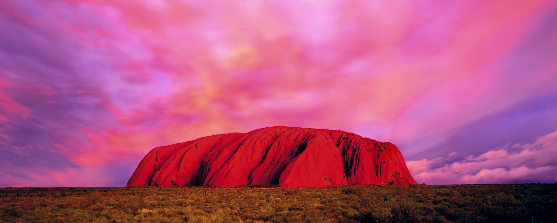 Ulurua ved solnedgang, med lyserøde og lilla skyer som den lyse røde klippe