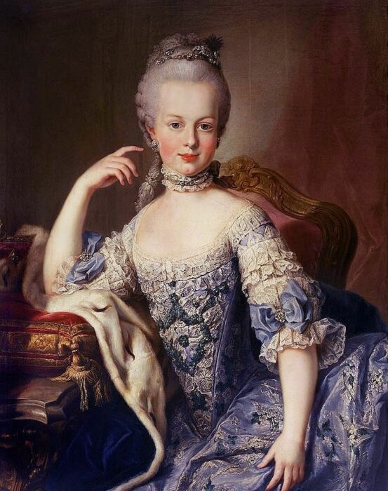 A painting of a young Marie Antoinette reclining on a low sofa wearing a gown of blue and white with her hair pulled back from her face and coiffed high upon her head.