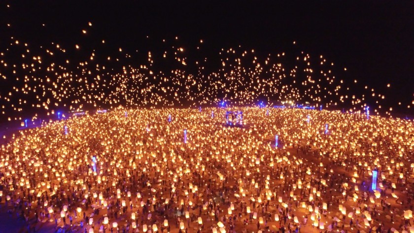 In een grote bijeenkomst laten mensen lantaarns los terwijl ze in een cirkel blijven, waardoor die plek een zeer grote verlichting krijgt.