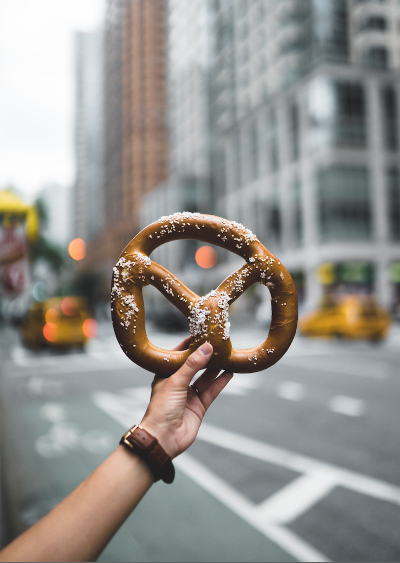 Someone holding a pretzel in front of an urban setting