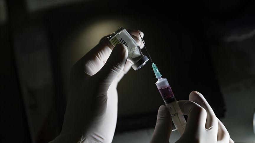 Gehandschoende handen van een medische professional die de naald van een spuit in een vileine plaatst die het vaccin bevat.