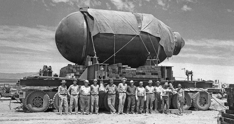 The Manhattan Project's first nuclear bomb, placed on a large stand, with members of the project standing in frotn of it in Lost Alamos, Mexico.