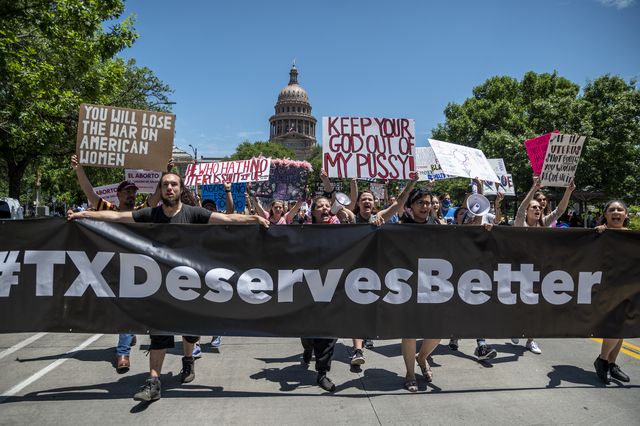 People protest on the road holding a large sign that says '#TXdeservesbetter'