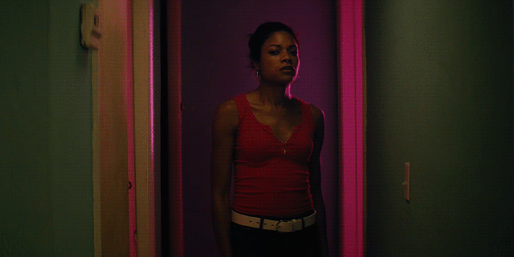 a woman walks slowly away from the camera and into a pink lit room.