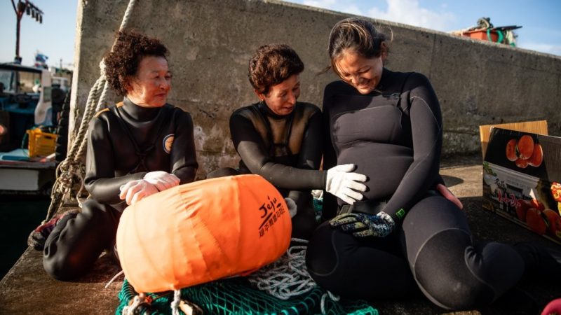a picture of three female divers sitting on the boat next to each other, one of the women is pregnant sitting at the right of the picture, the person next to her is touching her belly