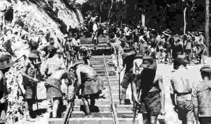 A black and white image of the early stages of building the railway, where POWs and Southeast Asian laborers are working hard in the sun, supervised by Korean and Japanese soldiers.