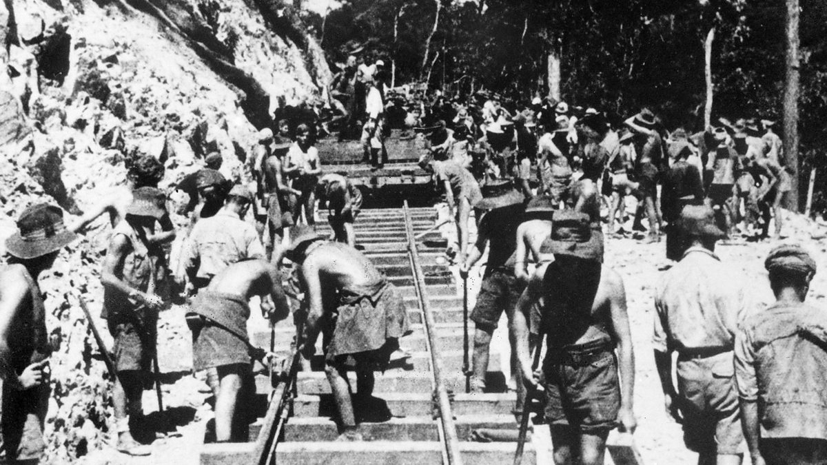 A black and white image of the early stages of building the railway, where POWs and Southeast Asian laborers are working hard in the sun, supervised by Korean and Japanese soldiers.