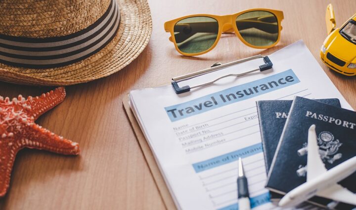 A table surface with a red starfish, a straw hat, orange sunglasses, two passports and a small toy areoplane, and a clipboard with a travel insurance form