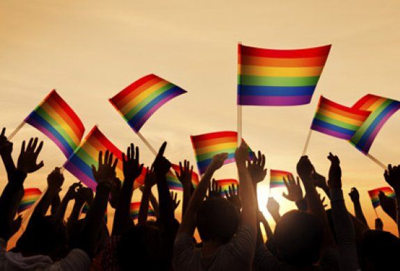 a cover image of multiple hands holding rainbow pridef flags against a sunset