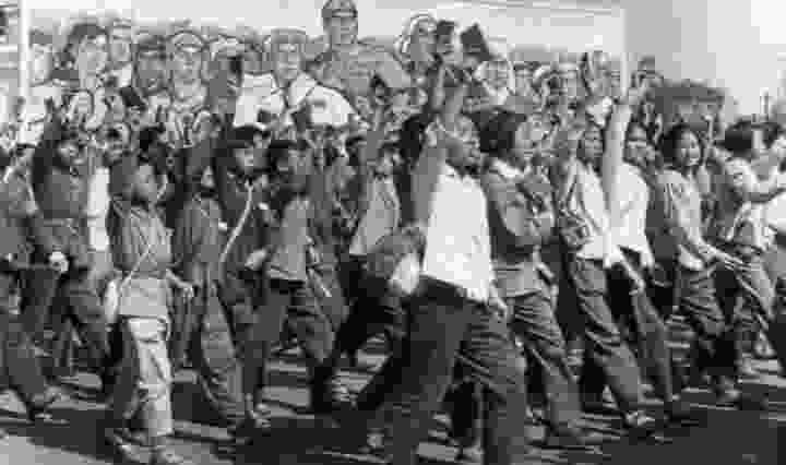 A black and white images of Chinese students, marching, while wearing the red armbands around their arms during the Cultural Revolution.