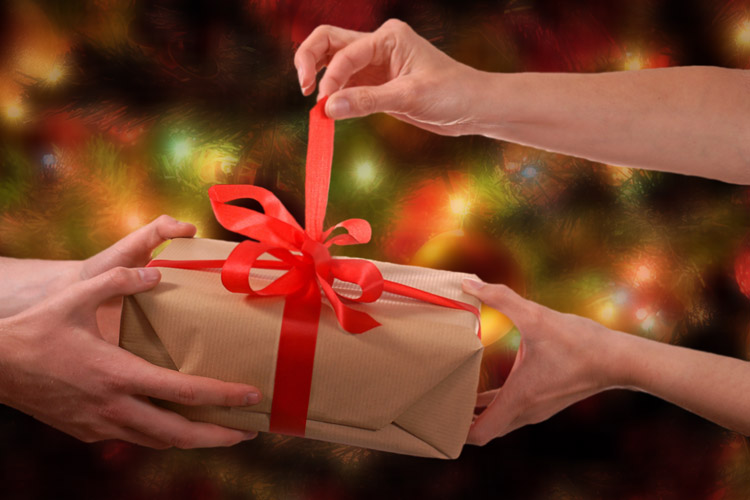 Two pairs of hands hold a brown paper wrapped present undoing the red ribbon