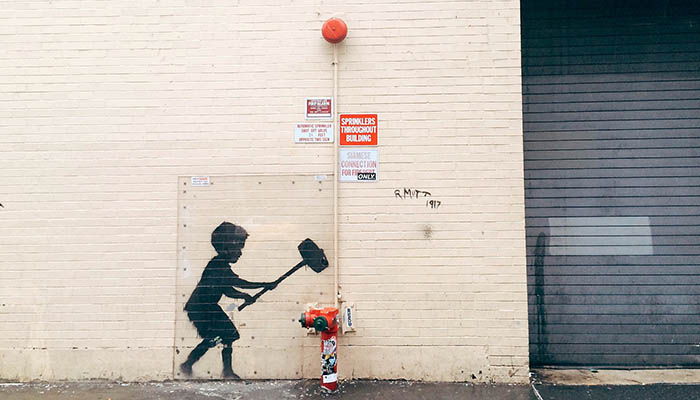 En dreng i silhuet med en hammer graffiteret på en cremefarvet væg