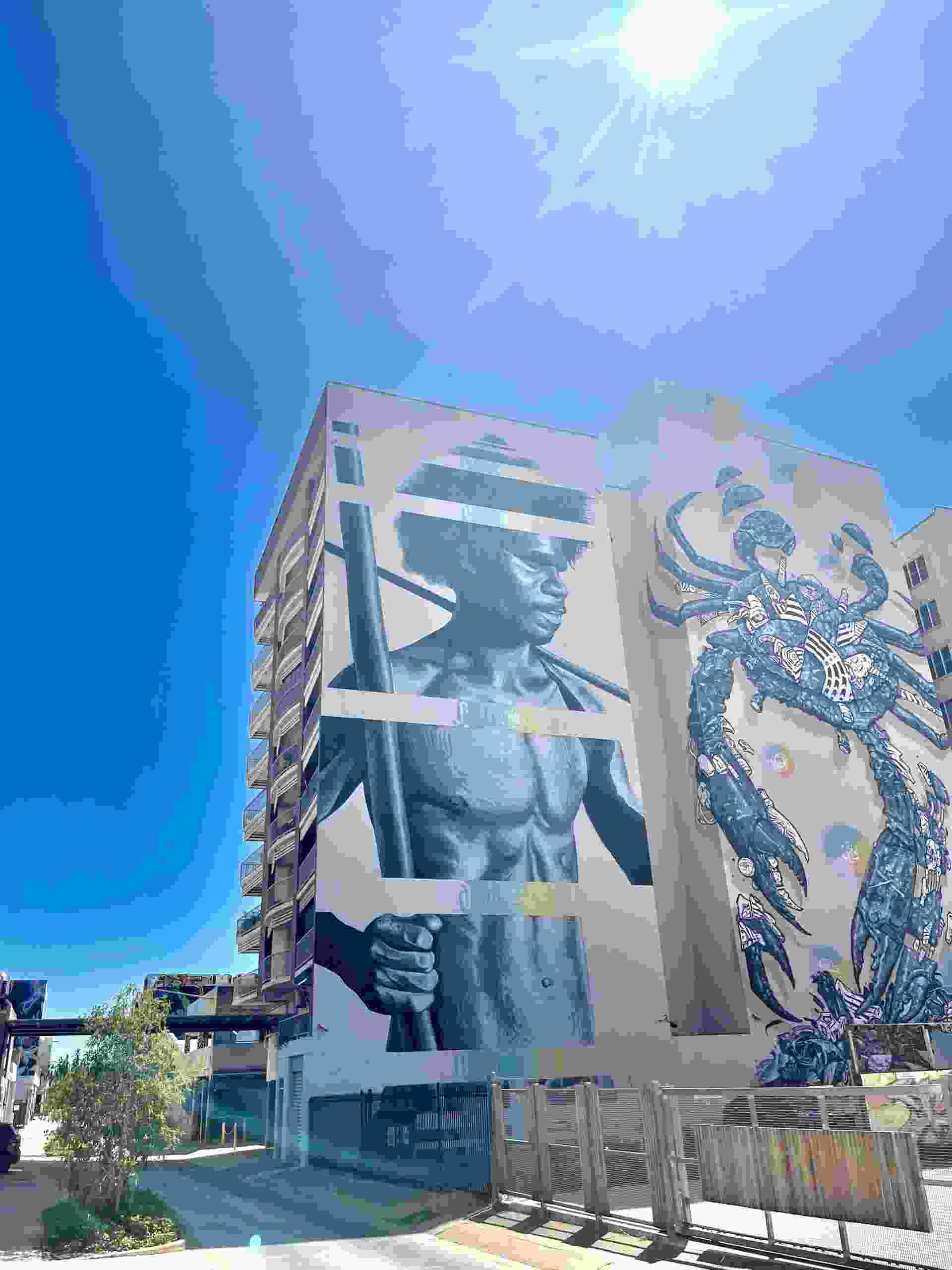 Блокова сграда в кремав цвят с увеличен мъж от първите нации, изобразен на стената