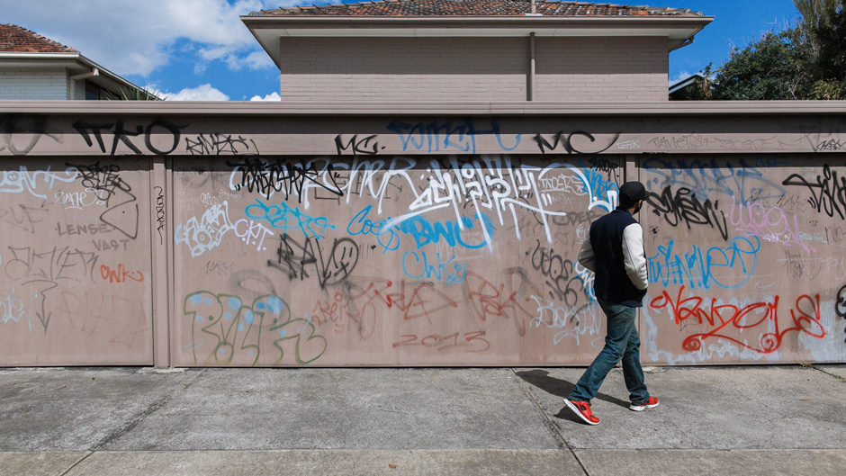 Mand går forbi en beige graffiti-mærket væg med hænderne i lommen