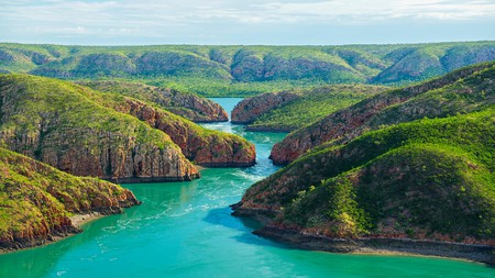 A turquoise blue river next to green mountains in the Kimberley.