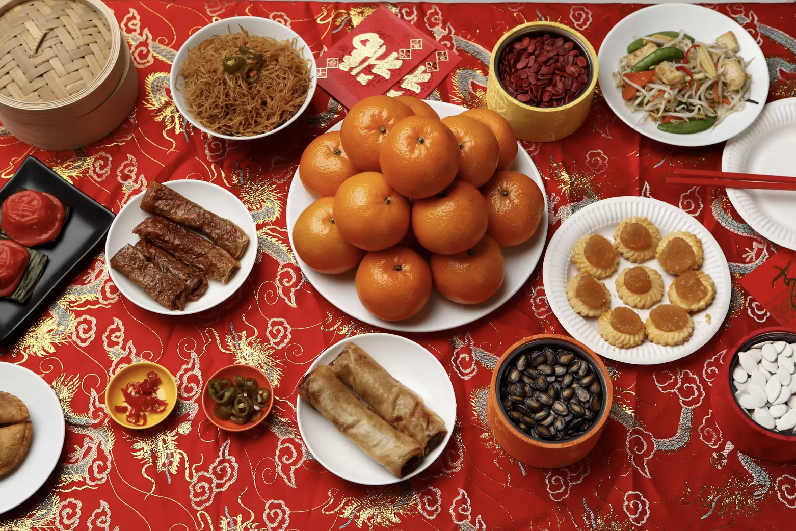 A red tablecloth covered in traditional Lunar New Year Chinese food, with oranges in the middle 