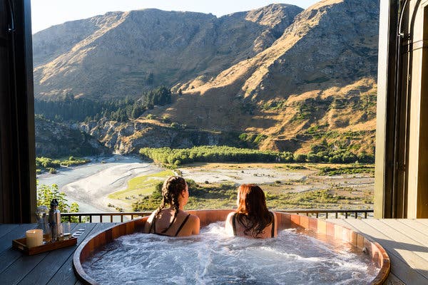 Two women sit in a hot tub overlooking the mountain scenery out a window in Queenstown New Zealand.