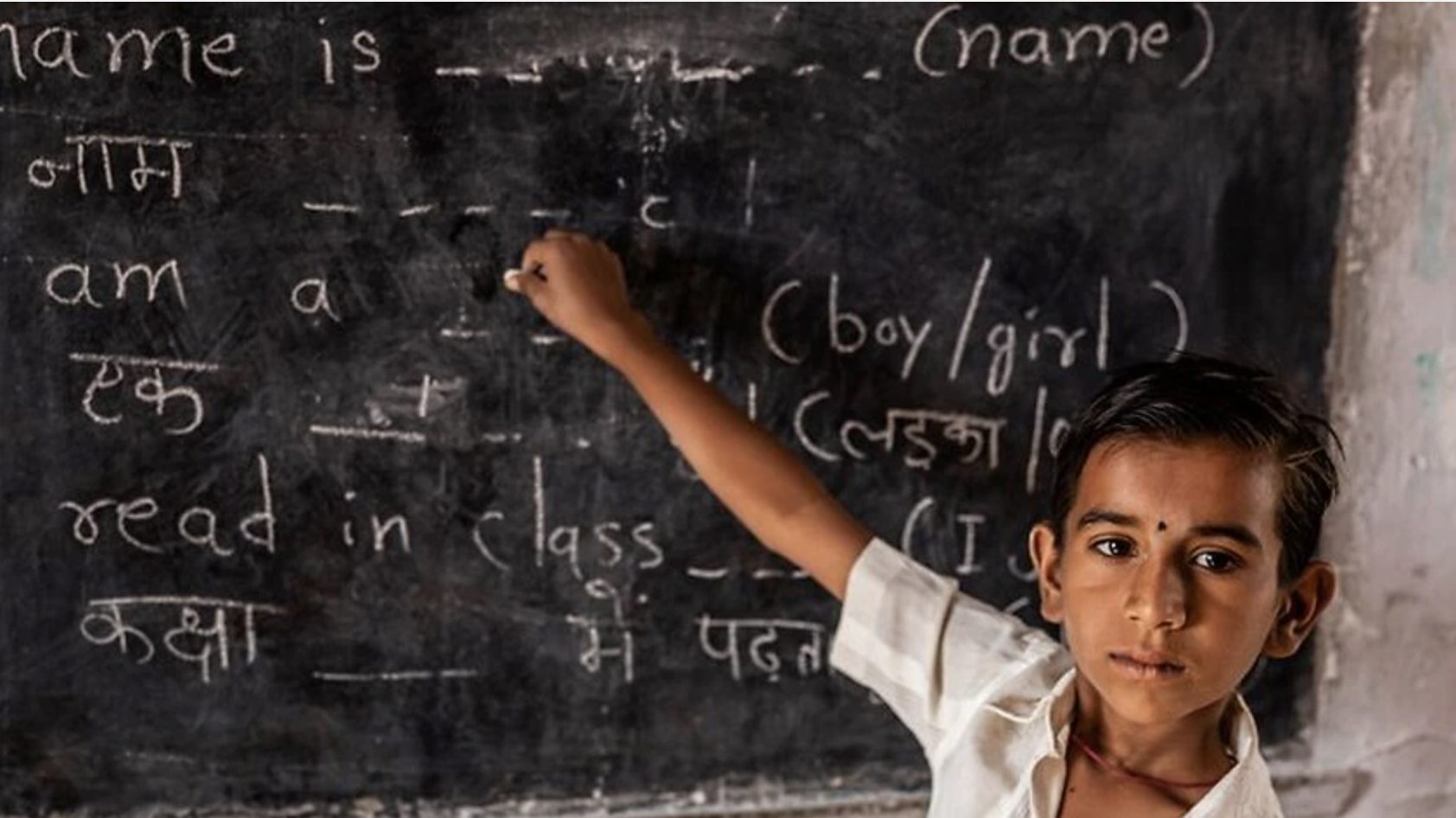 An Indian schoolboy is practicing English on the chalkboard with different English words