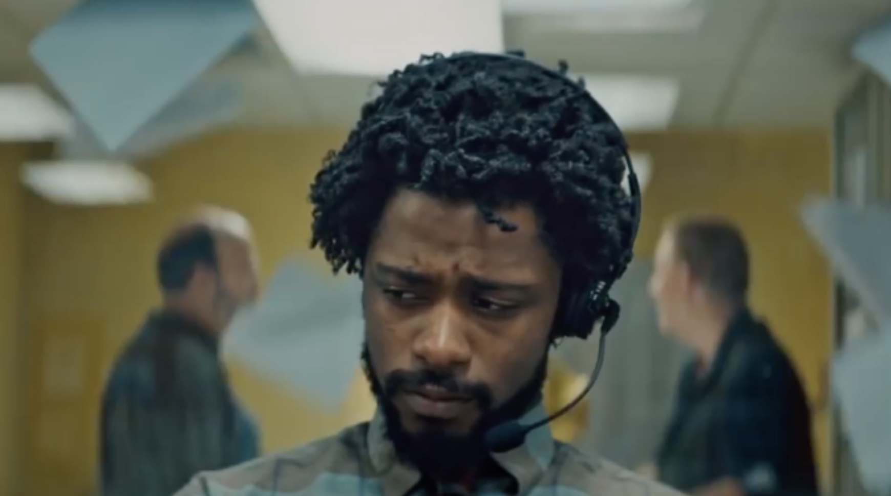 Scene from Sorry to Bother You, where a black telemarketer is in the foreground and beside him in the background are his white coworkers