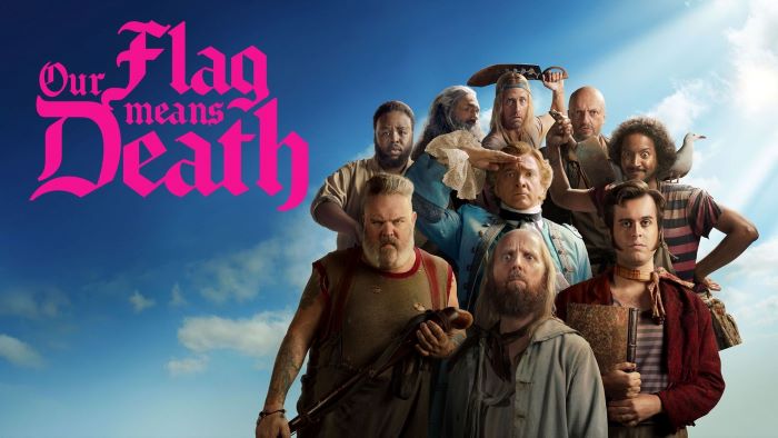Stede Bonnet and his crew stand at the ready against a sky-colored background. In pink letters, the title reads "Our Flag Means Death."