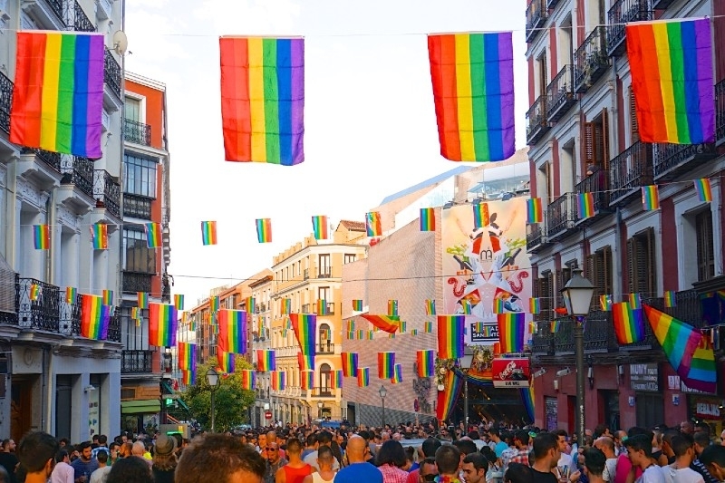 A street in Madrid, which is safe for LGBTQIA+ travelers, lined with rainbow flags and full of people. 