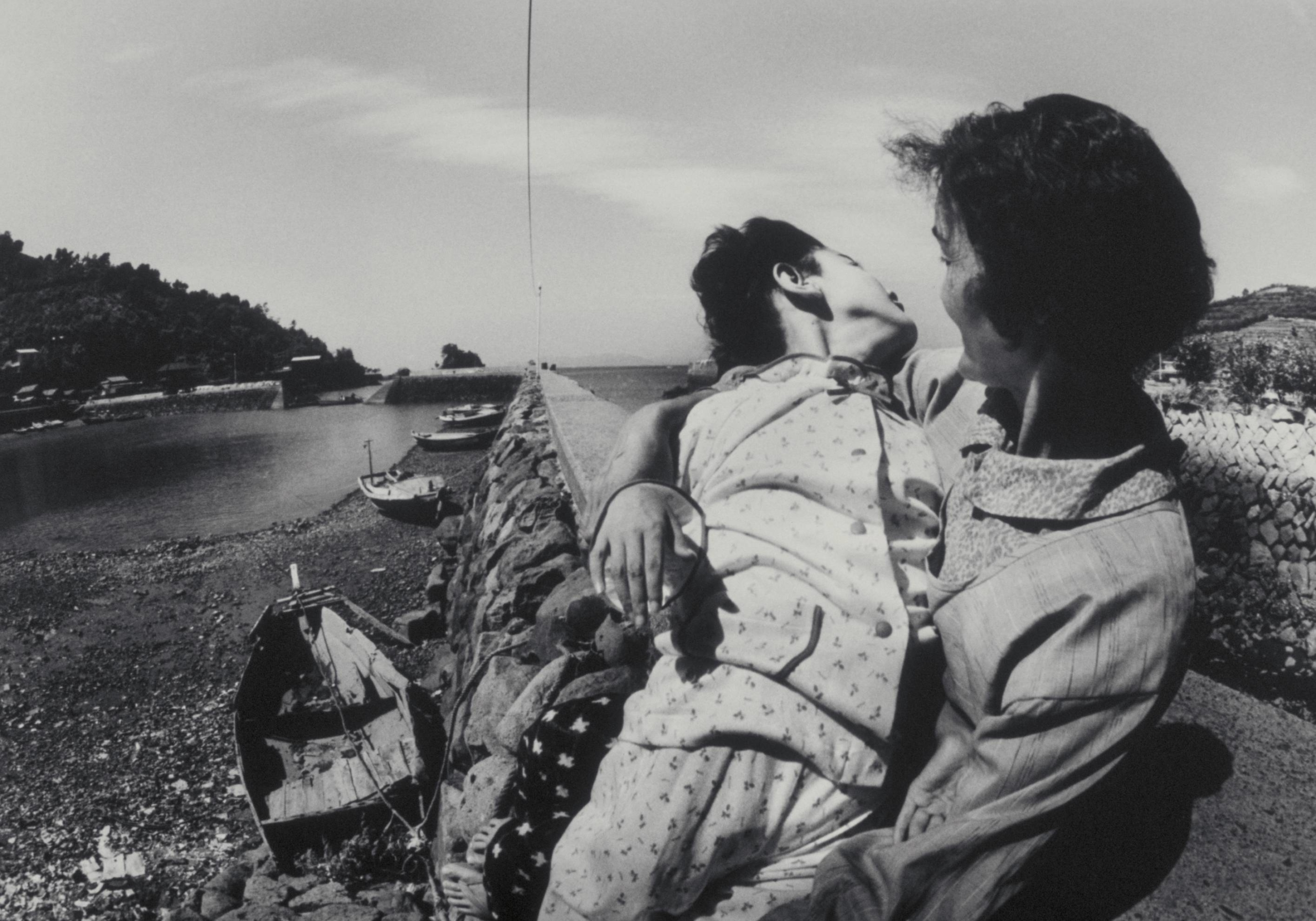 A black and white photograph of a mother holding her child, deformed from methylmercury poisoning, near the Minamata Bay.