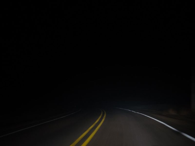 Un drum într-o noapte întunecată. Sunt vizibile doar linia mediană galbenă și o linie albă.
