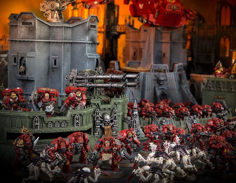 Diorama of a Warhammer 40K battlefield. Stalwart walls are manned by men in hulking power suits. They face off against a swarm of bug-like creatures.